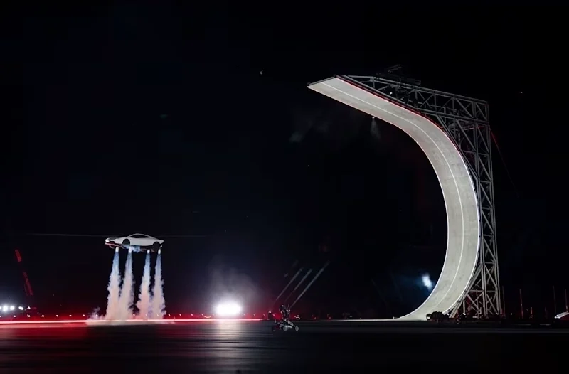 Demonstração do Tesla Roadster realizando uma manobra aérea com auxílio de propulsores, ao lado de uma estrutura de testes, destacando a proposta de levar tecnologias aeroespaciais ao universo automotivo.